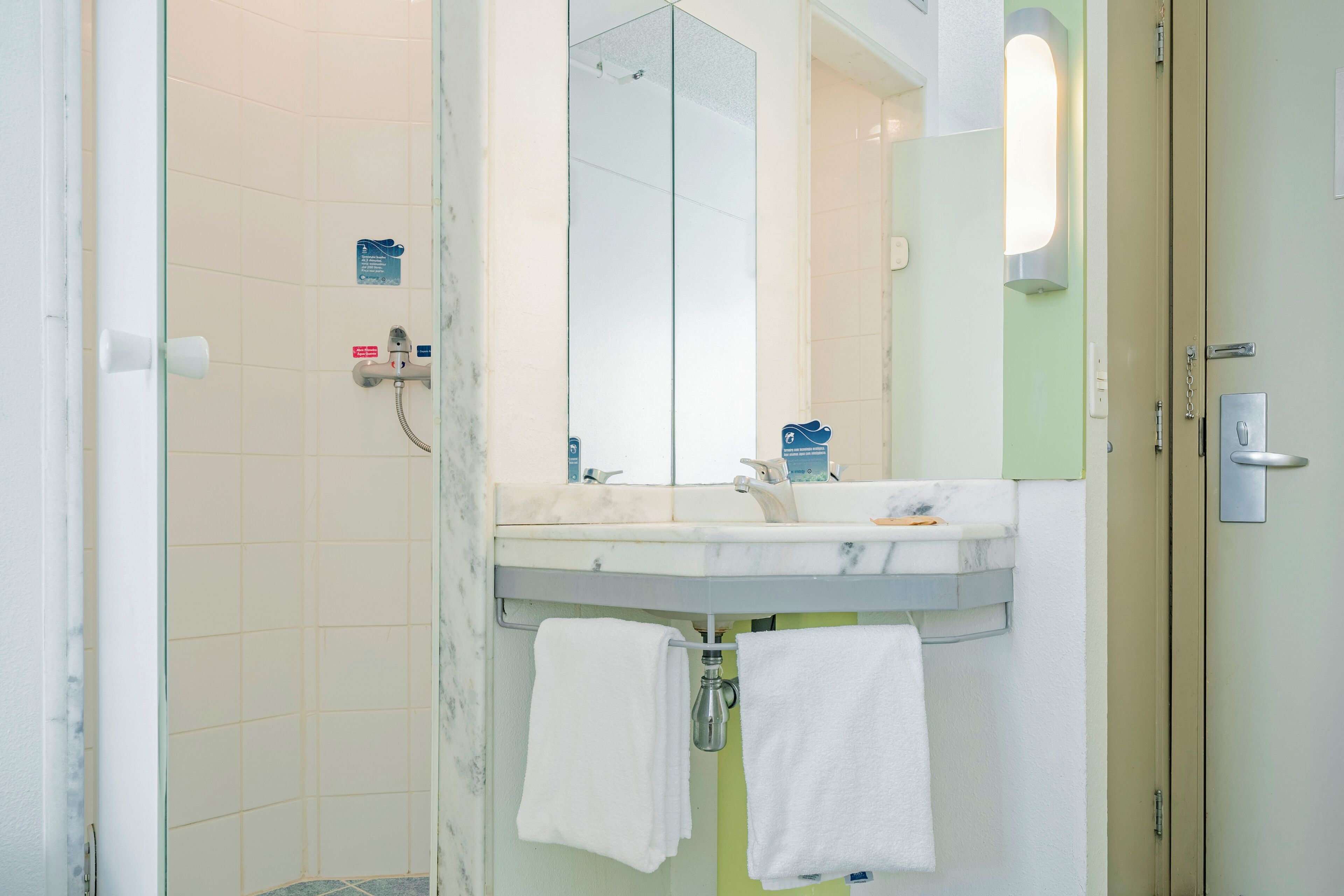 A bathroom with a glass shower enclosure, a sink with a mirror, and two towels hanging on hooks.