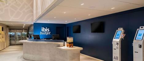 A reception area with a blue wall, a reception desk, two ATMs, and a refrigerator in the background.