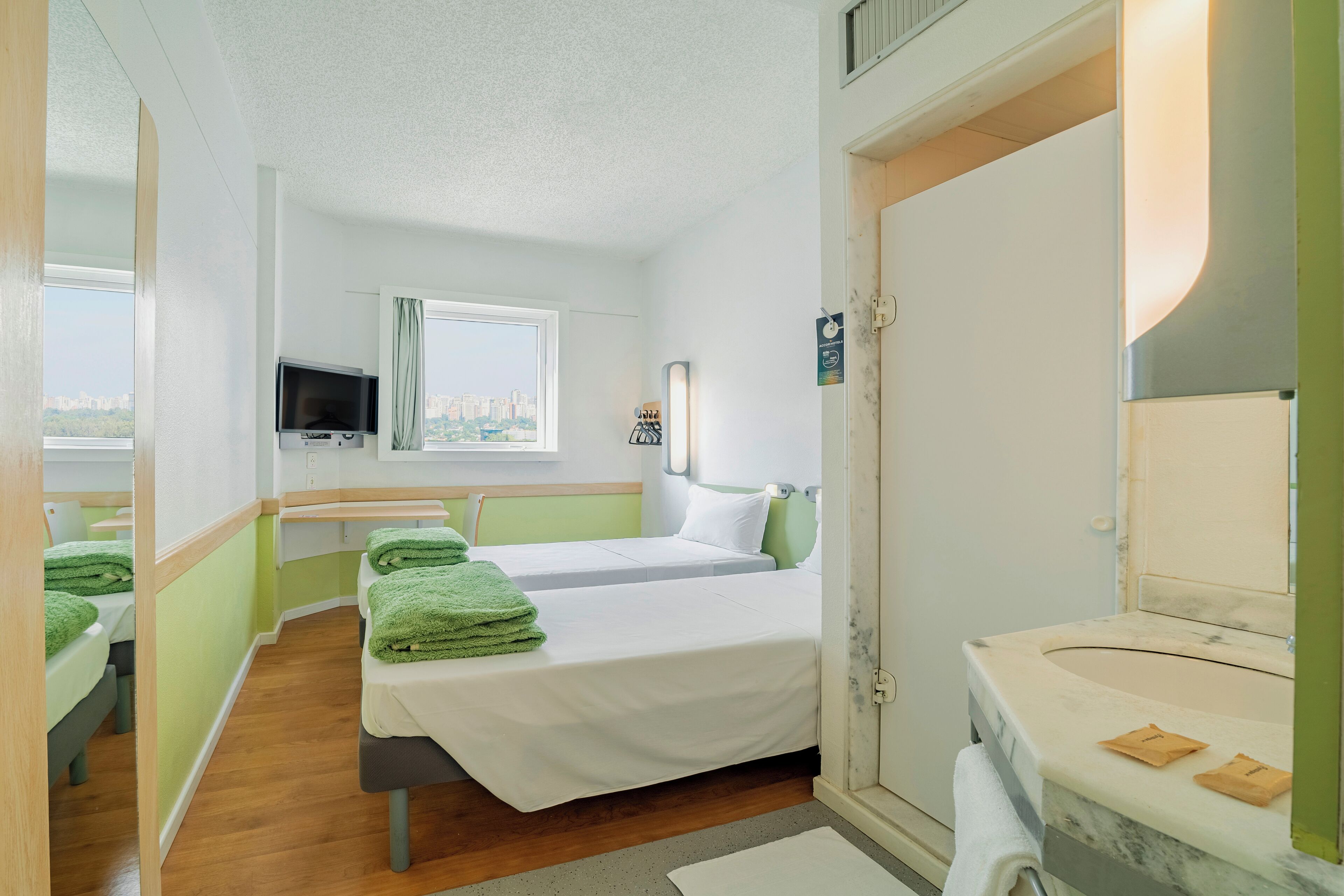 Hotelkamer met twee bedden, een televisie, een raam met uitzicht over de stad en een badkamer met een marmeren wastafel.