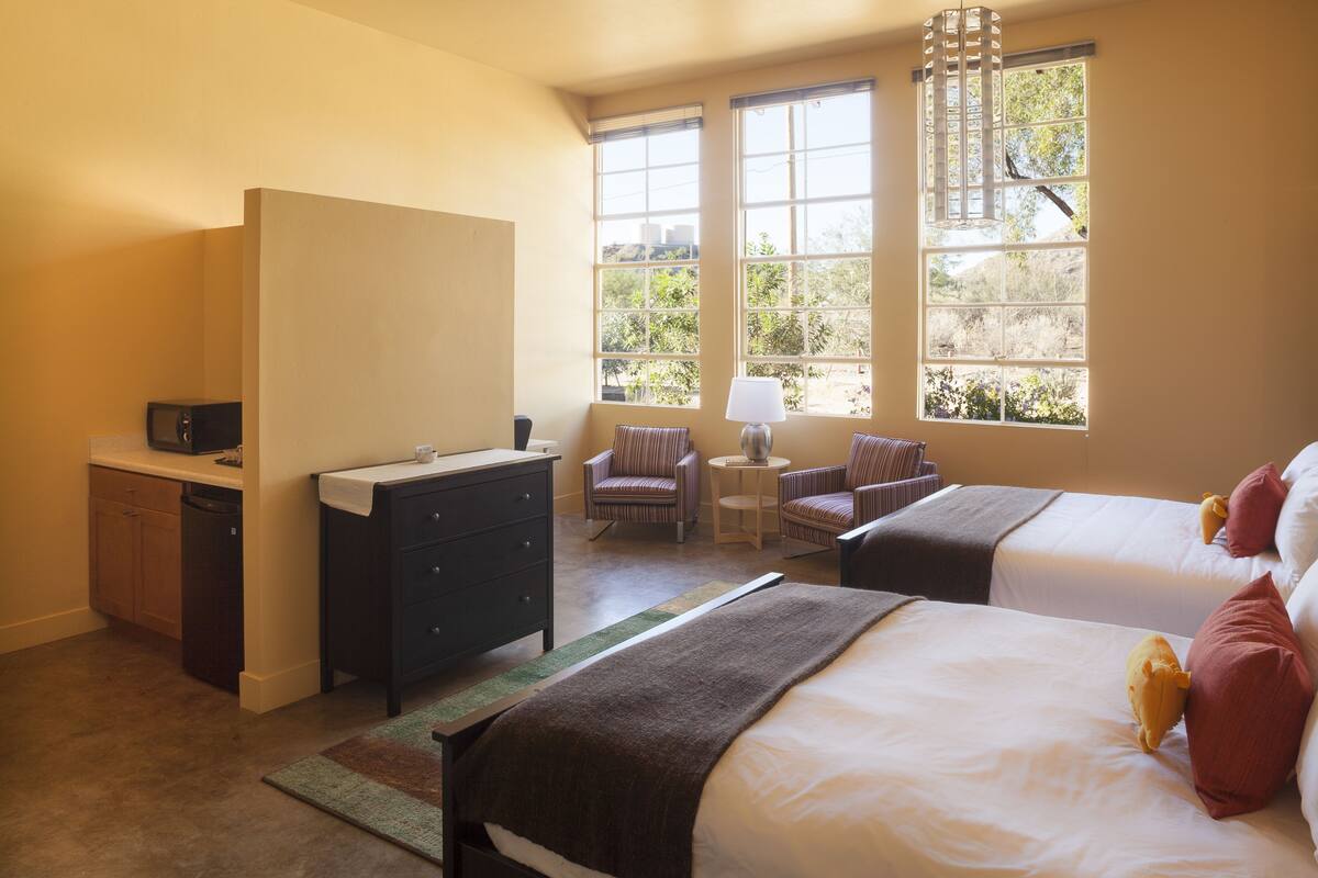 Habitación de hotel con dos camas, un escritorio, una silla y una ventana con vistas a árboles.