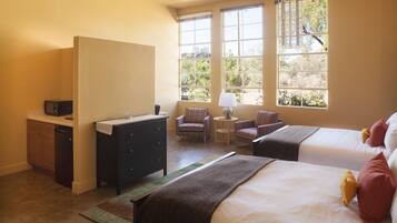 A hotel room with two beds, a desk, a chair, and a window with a view of trees.