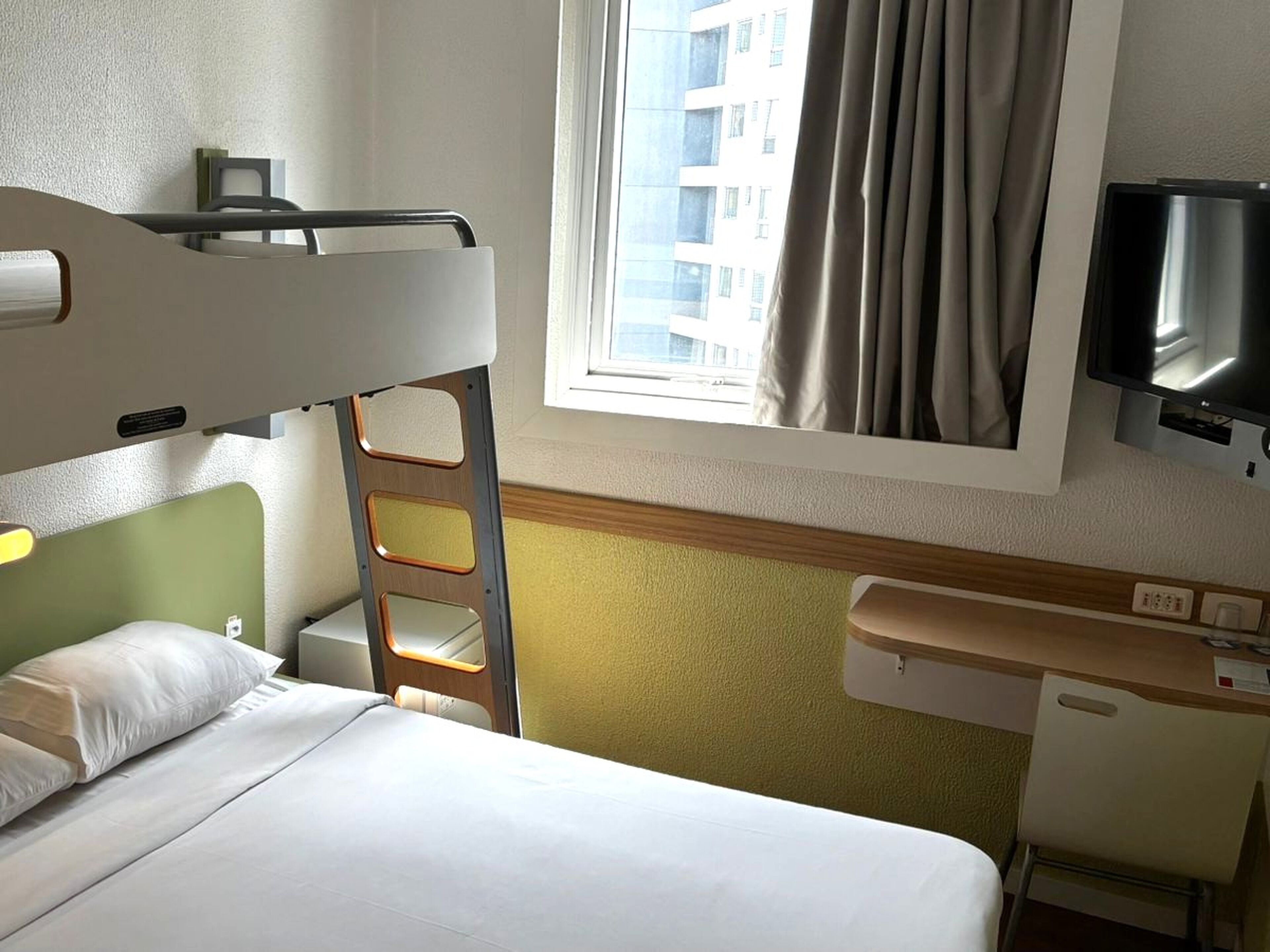 Una habitación de hotel con literas, un escritorio y una silla, un televisor y una ventana con cortinas.