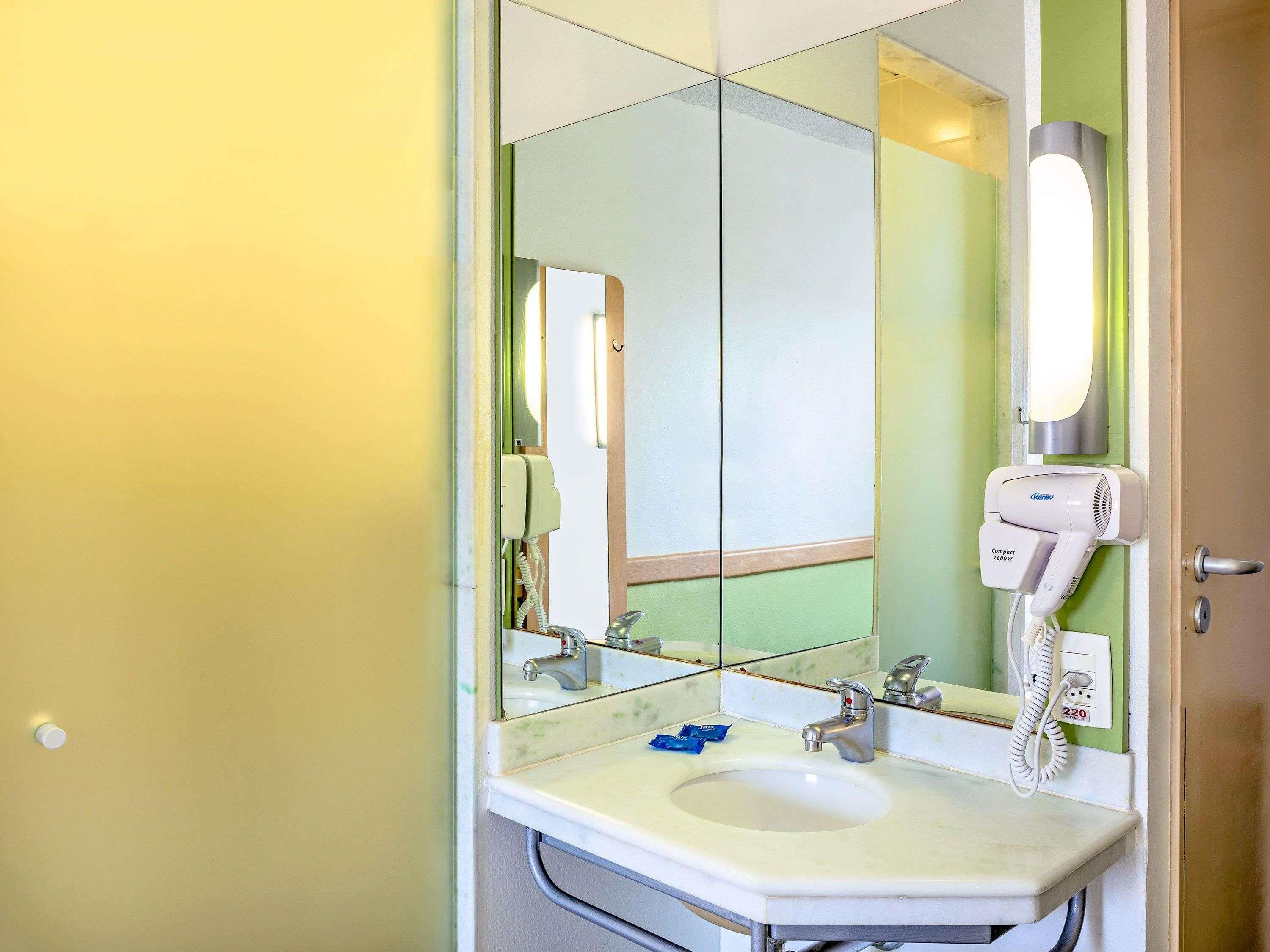A bathroom with a sink, mirror, hairdryer, and telephone.
