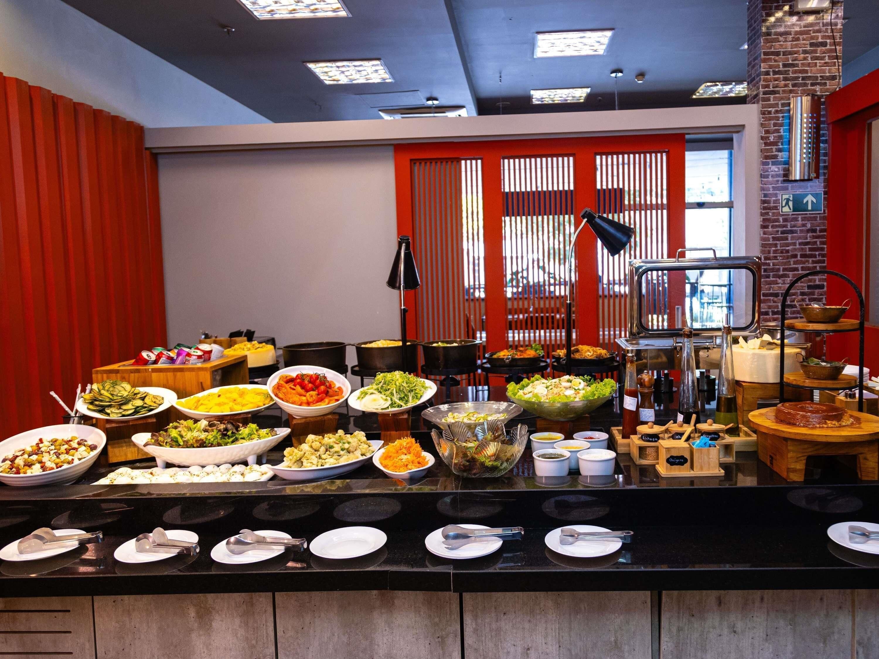 A buffet with various dishes and utensils, a brick wall, and a red curtain.
