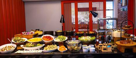 A buffet with various dishes and utensils, a brick wall, and a red curtain.