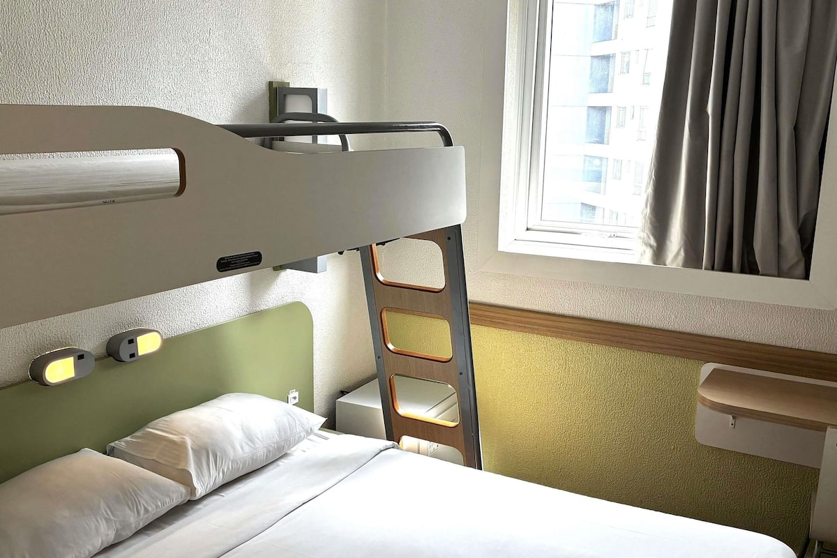 A hotel room with bunk beds, a desk, a chair, and a window with curtains.