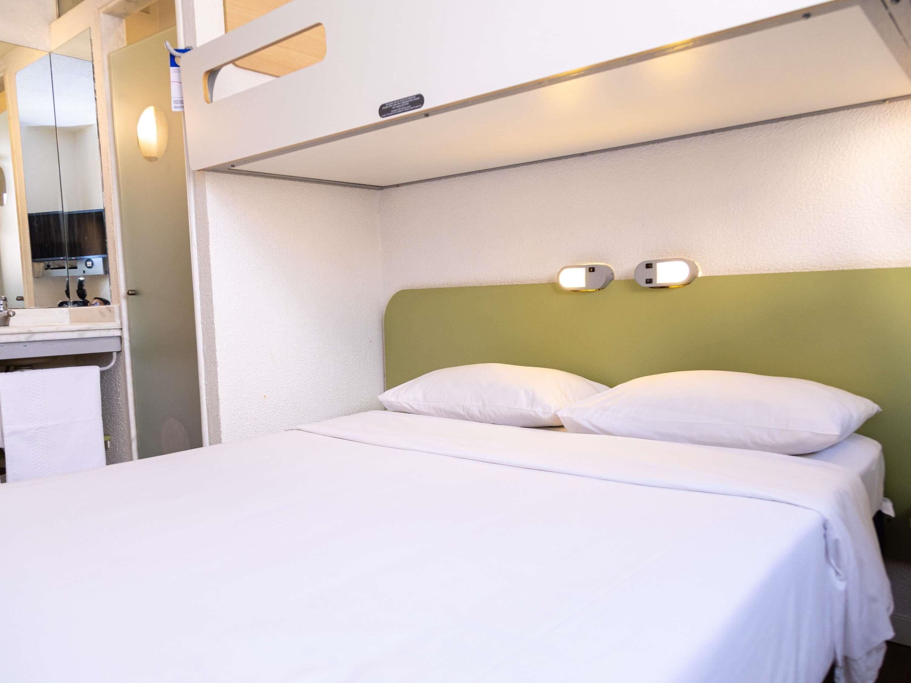 Una cama individual con ropa blanca, cabecera verde y dos lámparas de pared.
