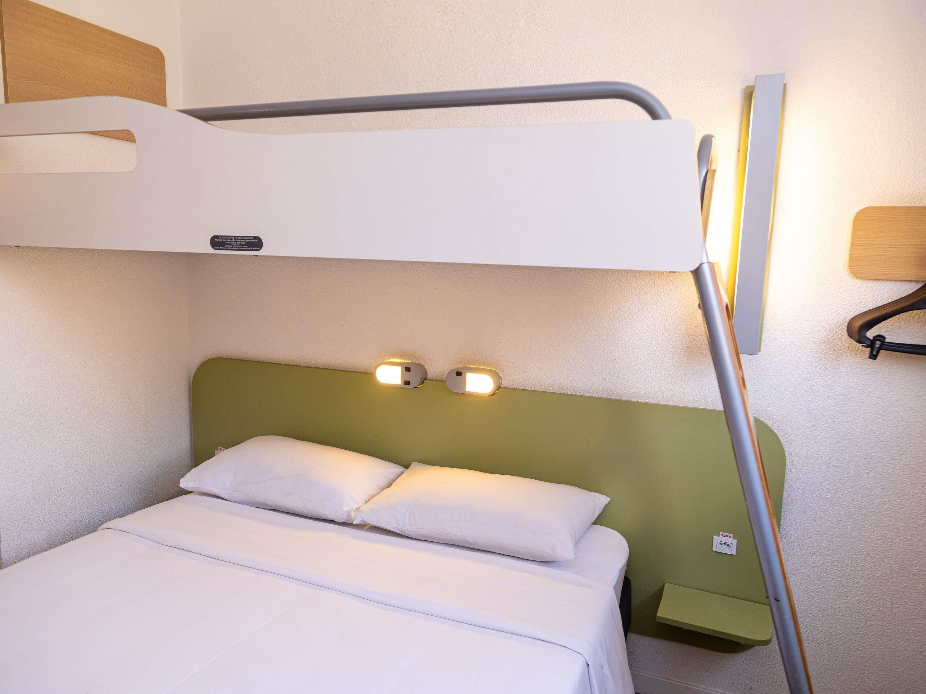 A bunk bed with a green headboard, two bedside lamps, and a small bedside table.
