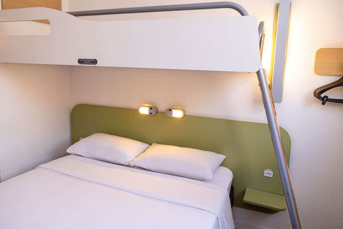 A bunk bed with a green headboard, two bedside lamps, and a small bedside table.