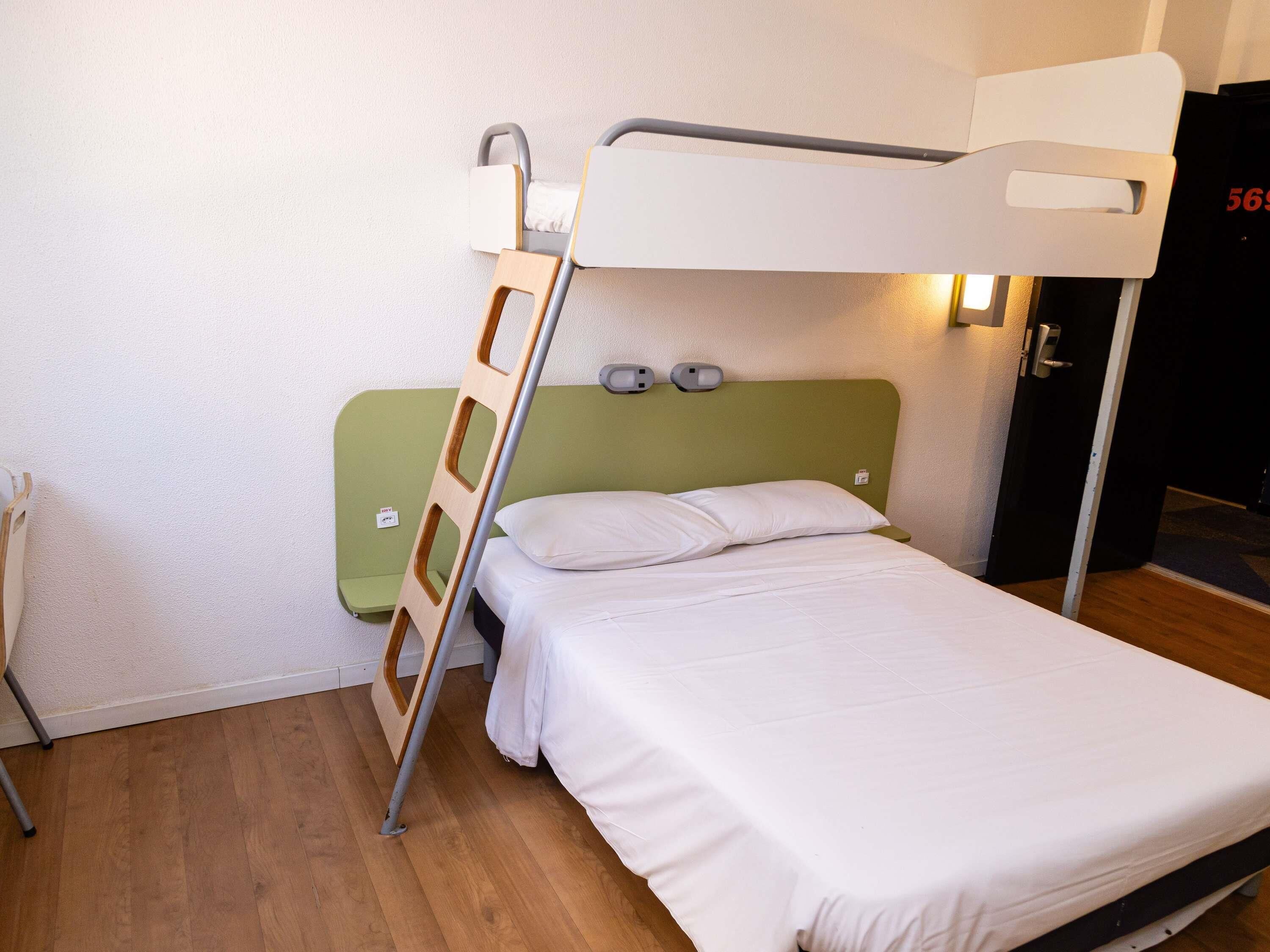 A bunk bed with a ladder, a green headboard, and a white mattress.