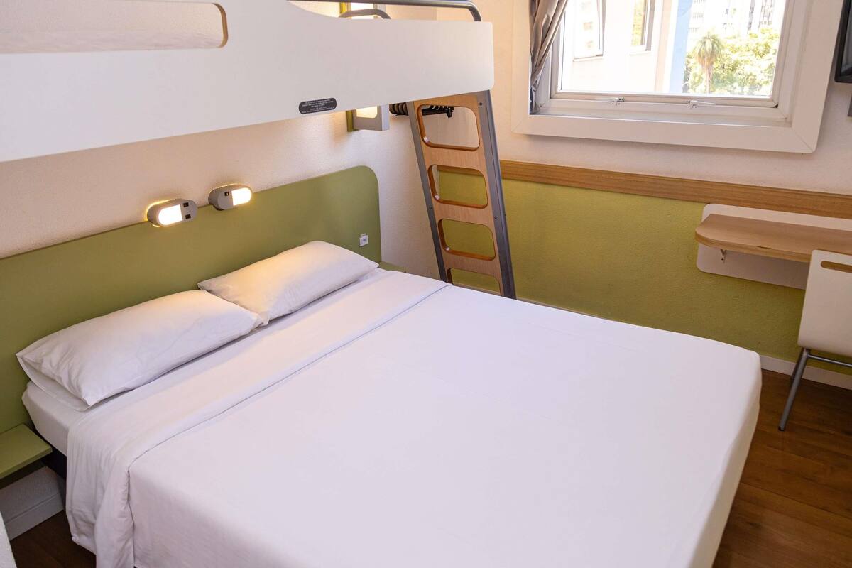 A bunk bed with a ladder, a desk, and a window with curtains.