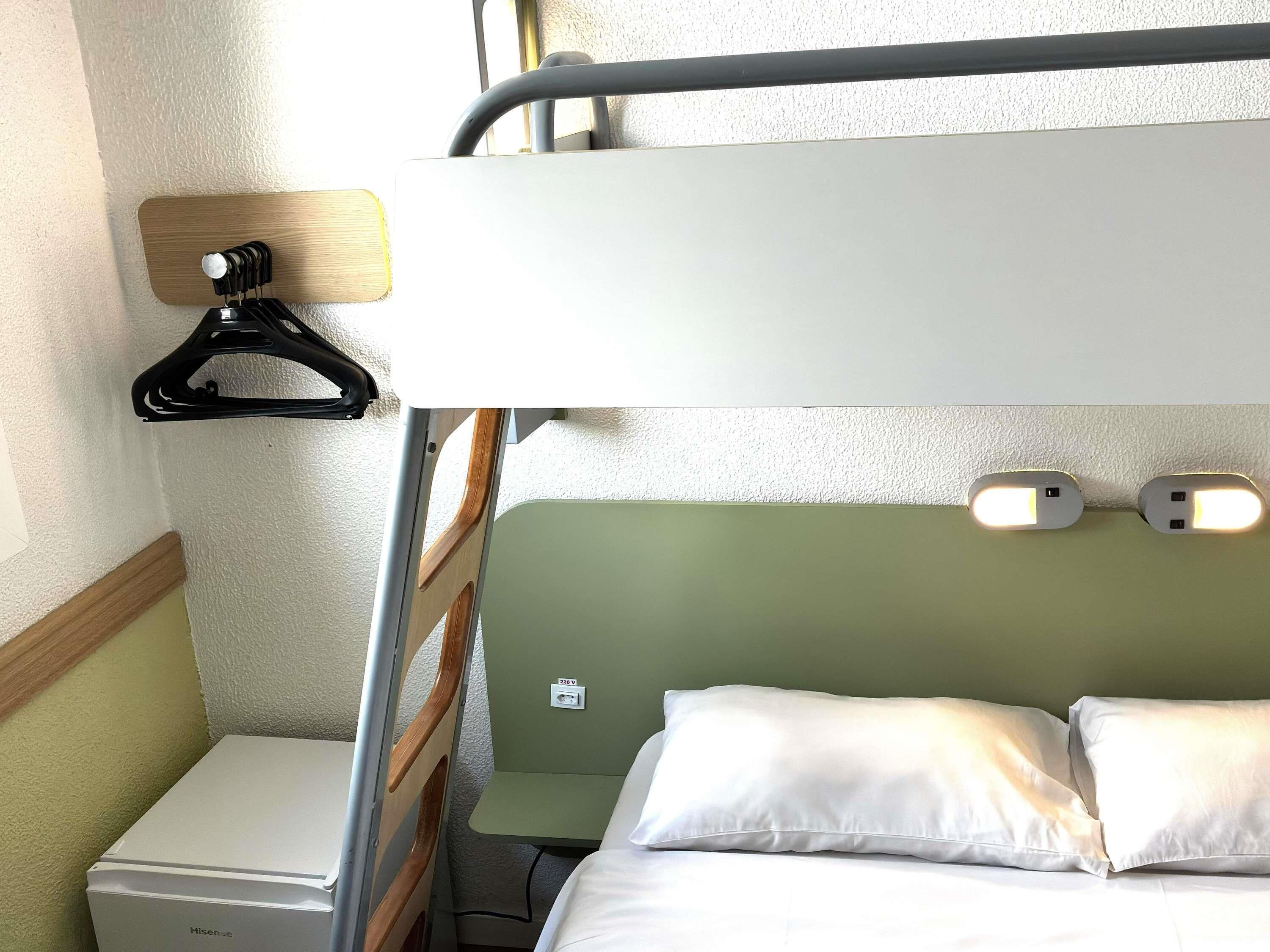Uma cama beliche com uma mesinha de cabeceira, um aquecedor e um ponto de luz fixado na parede.