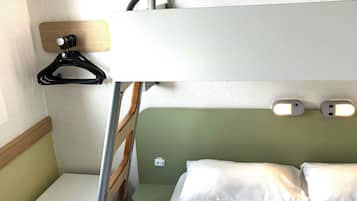 Uma cama beliche com uma mesinha de cabeceira, um aquecedor e um ponto de luz fixado na parede.