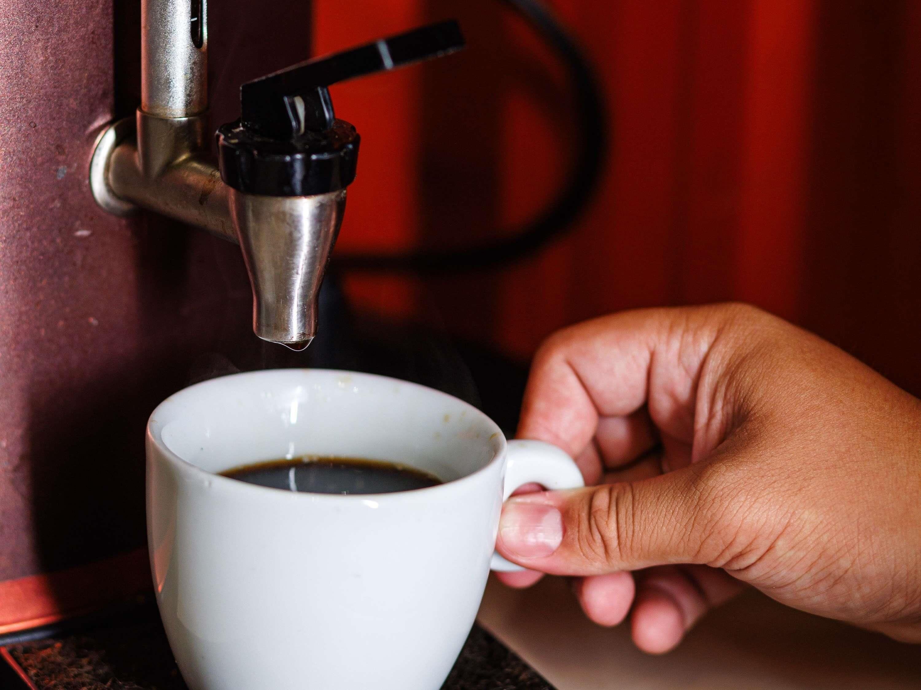 A hand holding a white cup under a coffee machine.