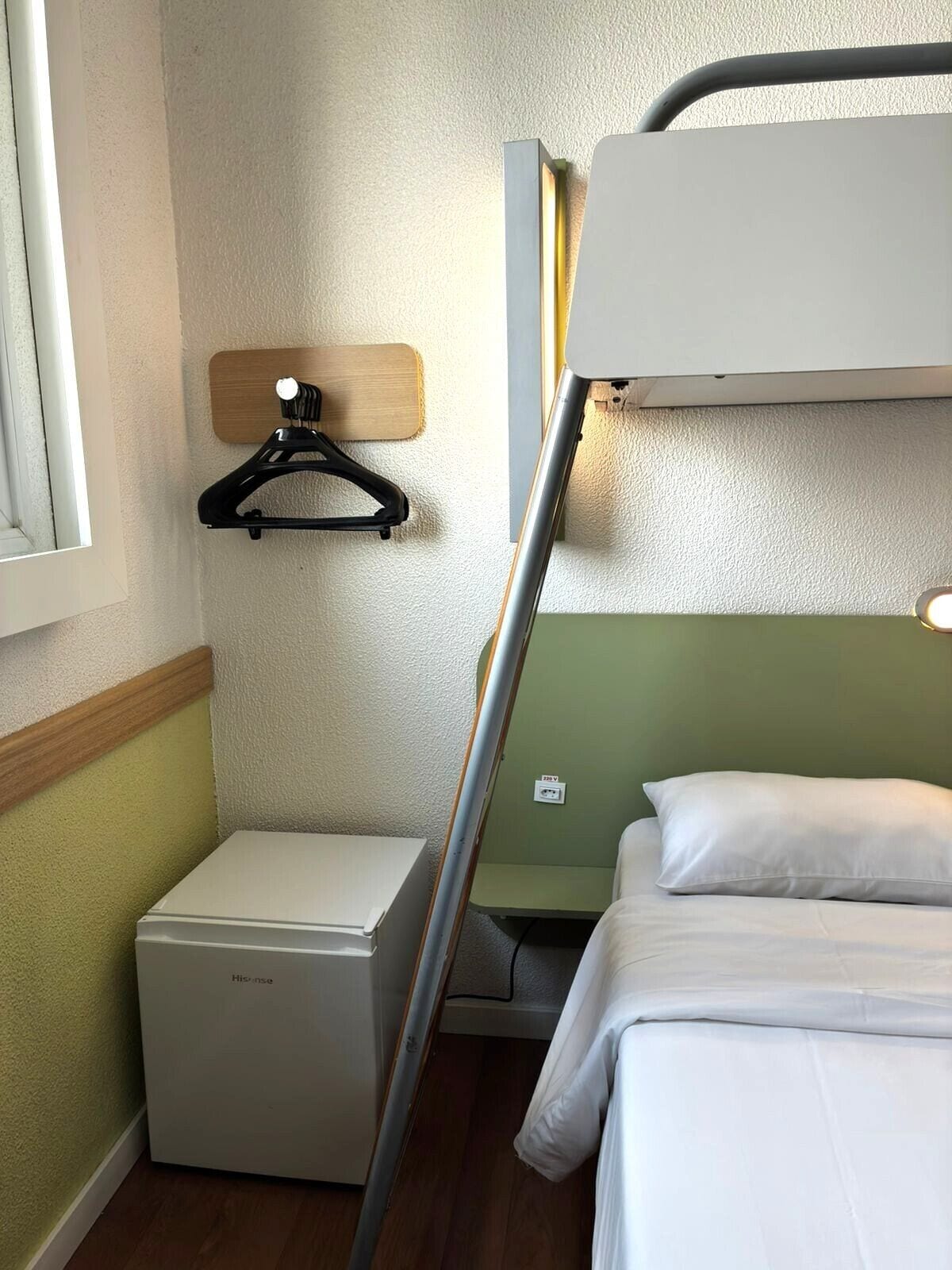 A bunk bed with a wooden headboard, a small bedside table, and a wall-mounted light fixture.