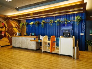 A hotel reception area with a blue curtain backdrop, a reception desk, seating, a trash bin, and a television screen. - ibis budget Belo Horizonte Minascentro (Belo Horizonte)