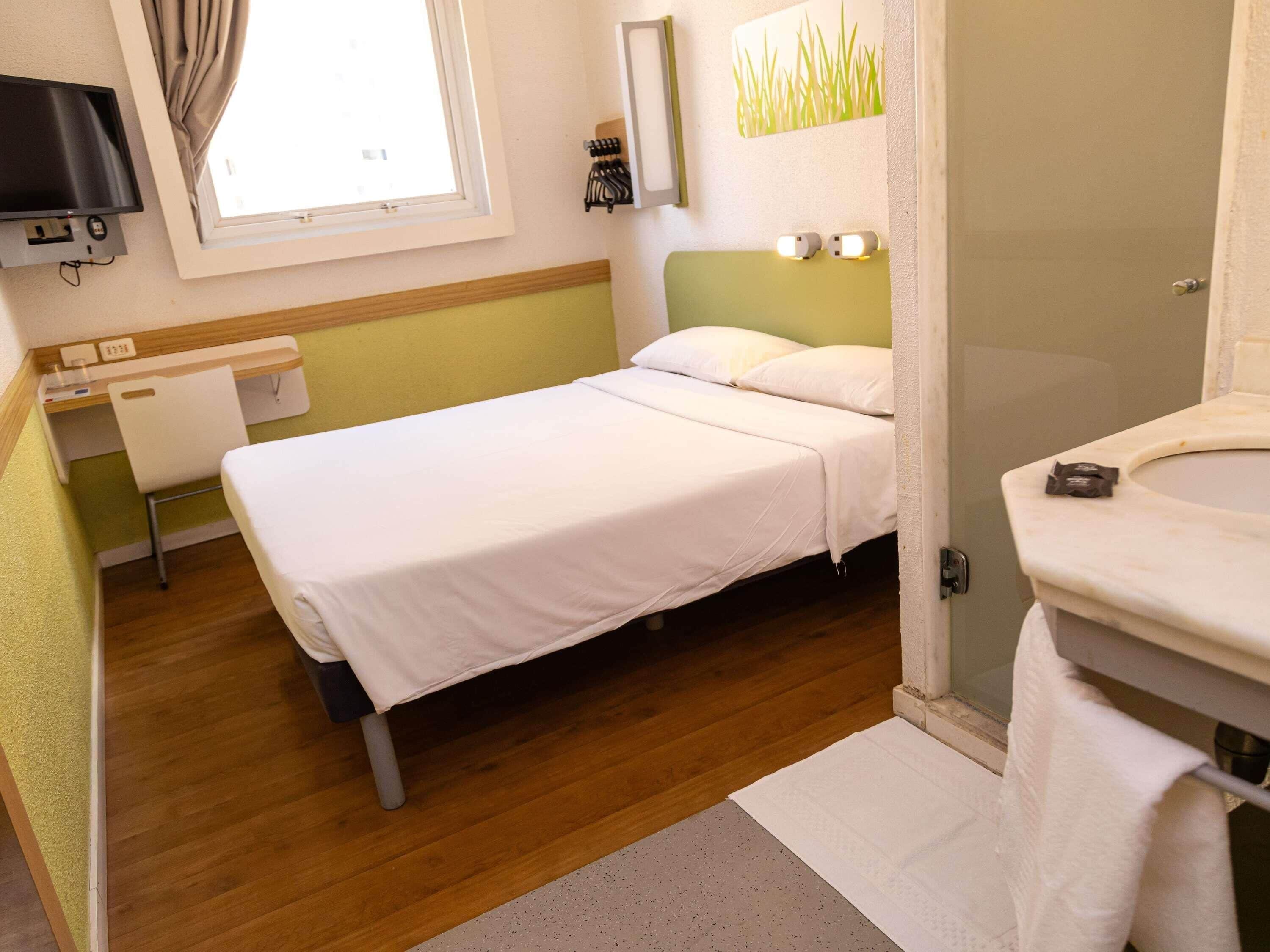 A small, clean room with a bed, a desk, a mirror, and a bathroom.