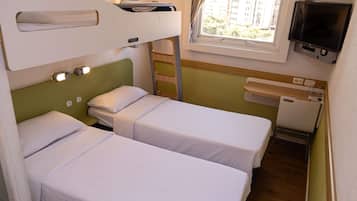 Una habitación de hotel pequeña y funcional con literas, televisión, ventana con cortinas y un escritorio pequeño con silla.