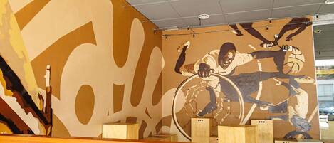 A modern interior with a large abstract mural, wooden seating, and a ceiling with recessed lighting.
