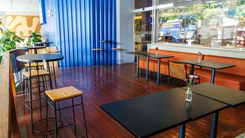 A restaurant interior with wooden flooring, black tables, and orange seating.