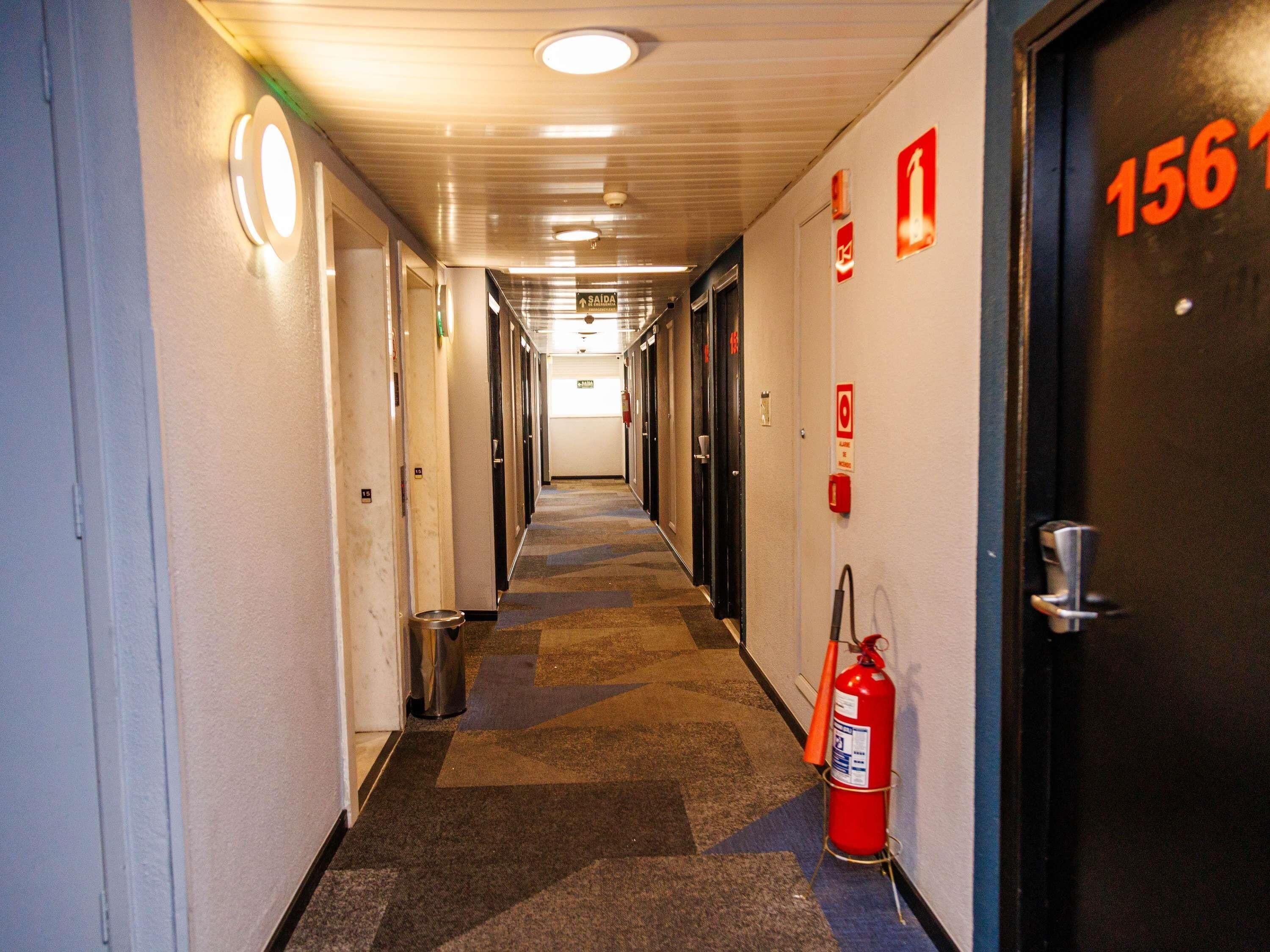 Ein Hotelgang mit Türen mit den Nummern 156, Feuerlöschern und einem Mülleimer.