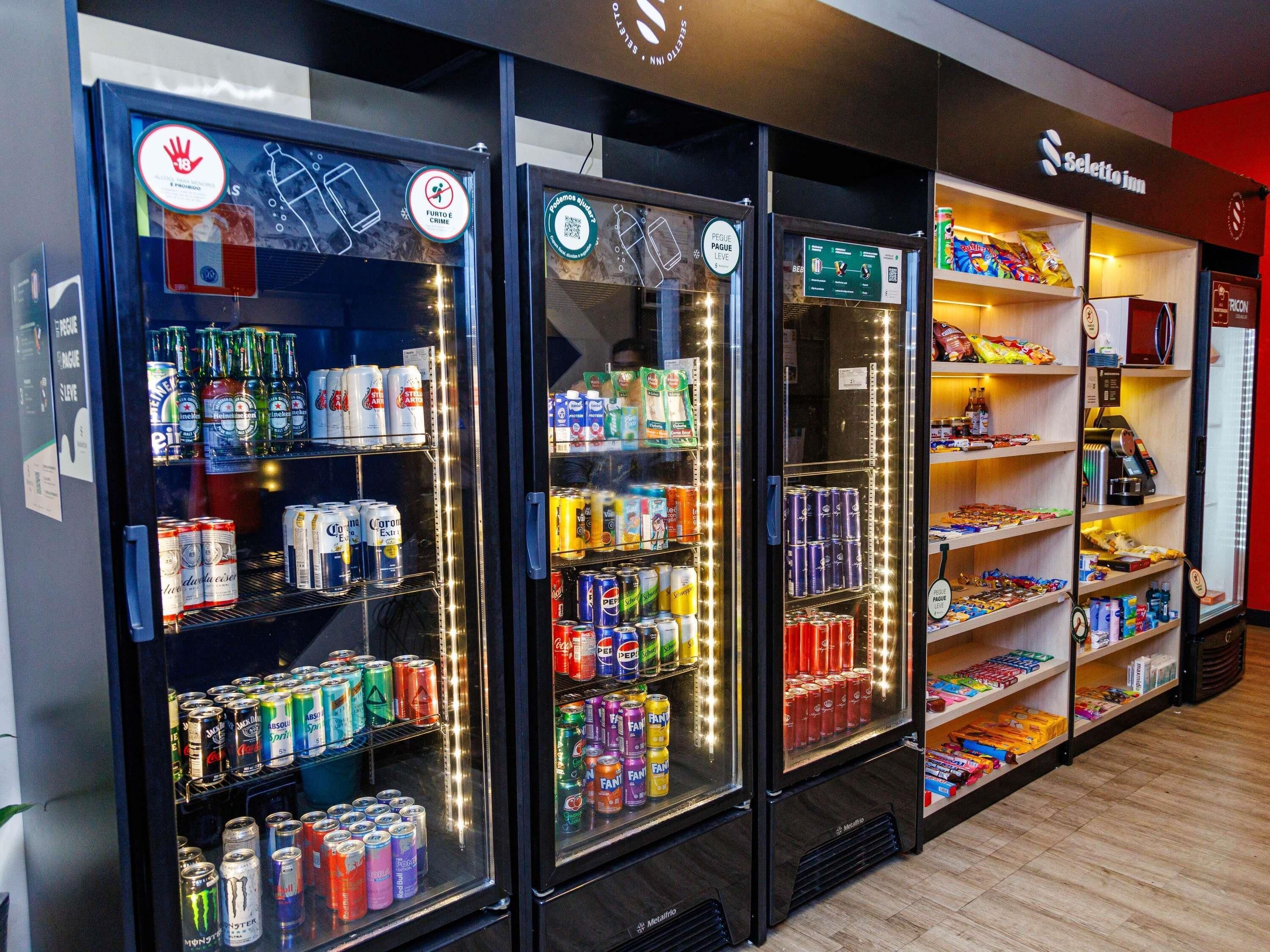 Trois distributeurs automatiques de boissons proposant une variété de choix, et une étagère à provisions située à droite.