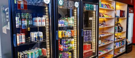 Tres máquinas expendedoras de bebidas con diversas opciones y un estante con aperitivos a la derecha.