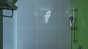 Un baño con azulejos blancos, una pared verde, una ducha con cabezal de ducha manual y un perchero con una toalla.