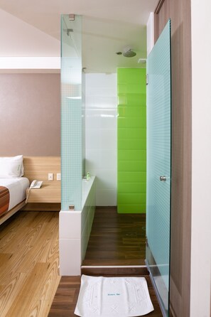 Relax in a stylish room with a comfortable bed, glass partition, and modern bathroom featuring a shower enclosure and sink.