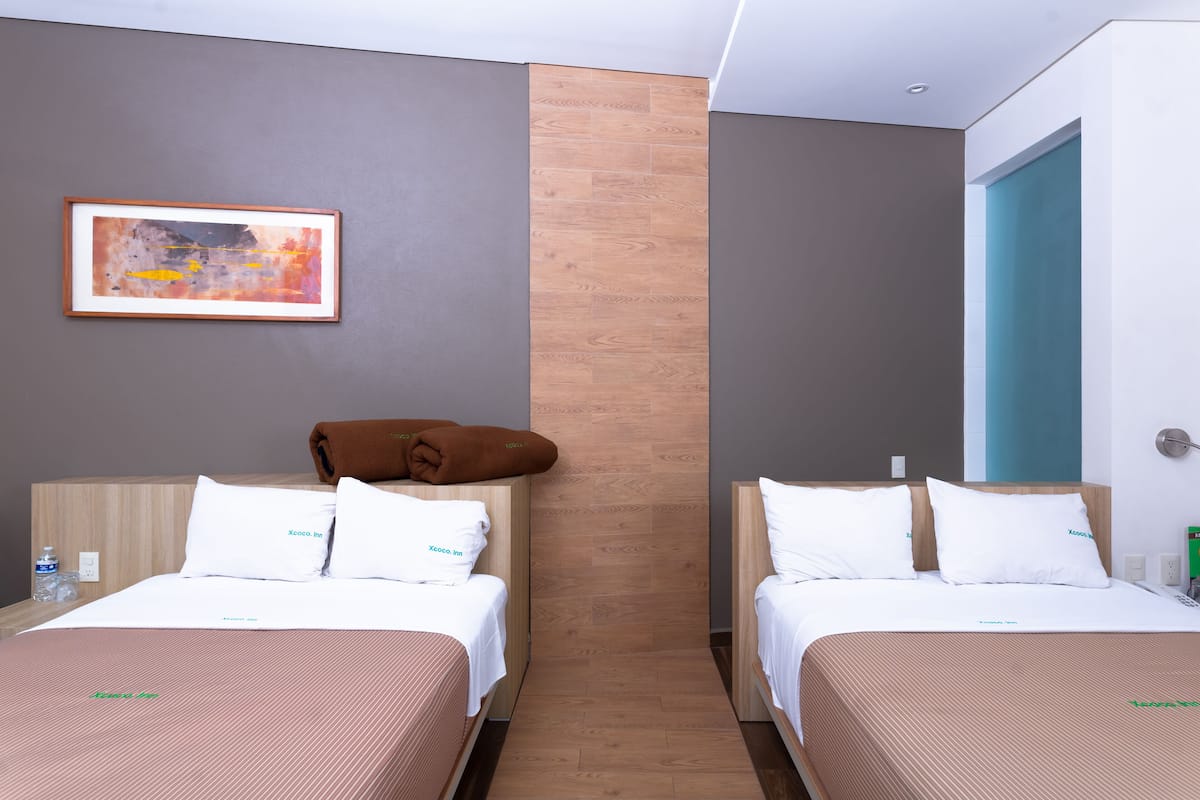 A hotel room with two beds, a framed abstract painting, and a wooden accent wall.
