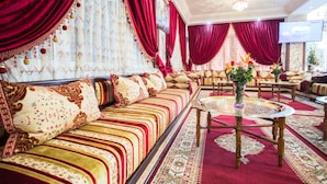 A luxurious room with a long sofa, multiple chairs, a round coffee table, and a TV screen. - Les Ambassadeurs Appart Hotel (Marrakech)