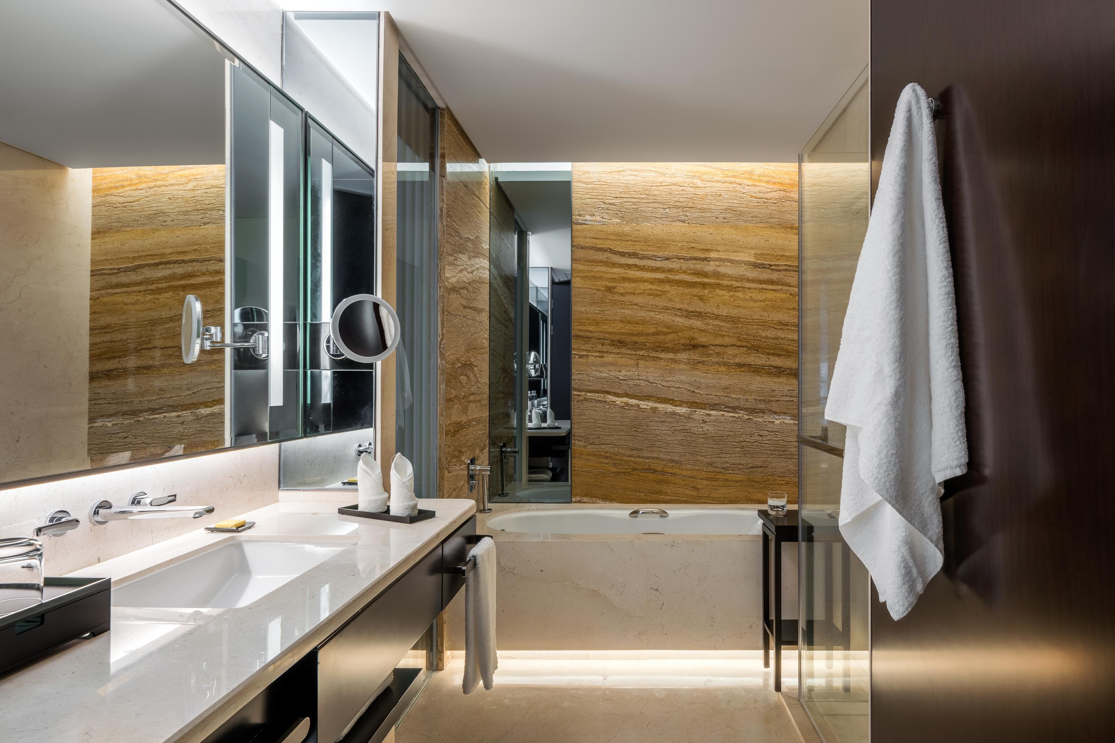 Un baño moderno con un espejo grande, lavamanos dobles, bañera y una toalla colgada en la pared.