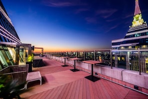 Terraza en la azotea con mesas y sillas, que ofrece vistas a la ciudad al atardecer.