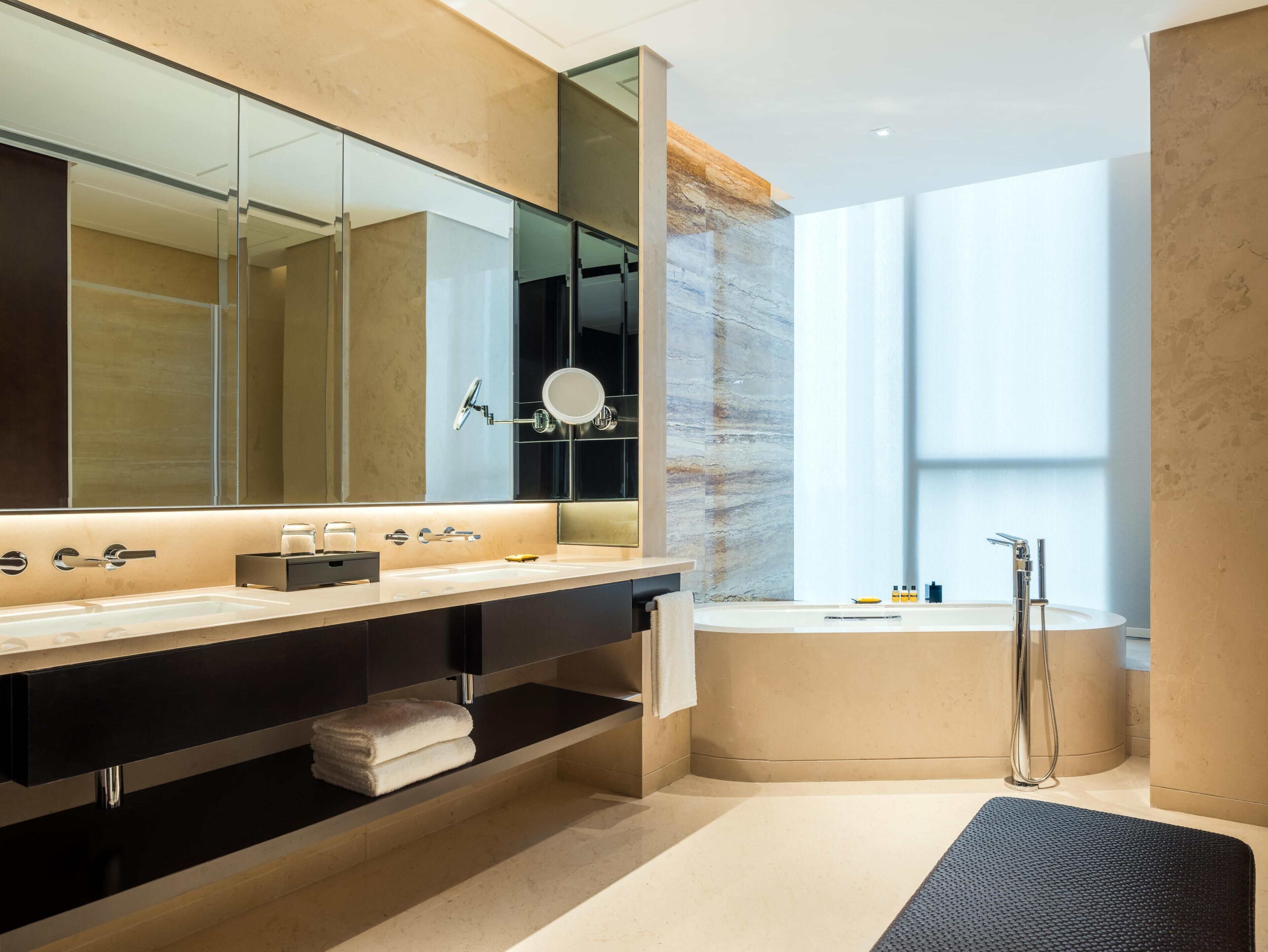 A modern bathroom with a large mirror, a bathtub, and a vanity with a sink.