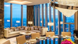 A modern hotel room with a large sofa, dining table set for four, and a city view through floor-to-ceiling windows. - Hyatt Regency Shanghai Global Harbor (Shanghai)