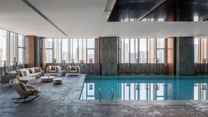 Amplia zona de piscina interior con vistas despejadas del horizonte urbano a través de grandes ventanales.