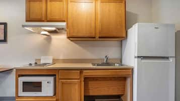 Eine kleine Küche mit Holzschränken, einer eingebauten Mikrowelle, einem Spülbecken und einem weißen Kühlschrank.