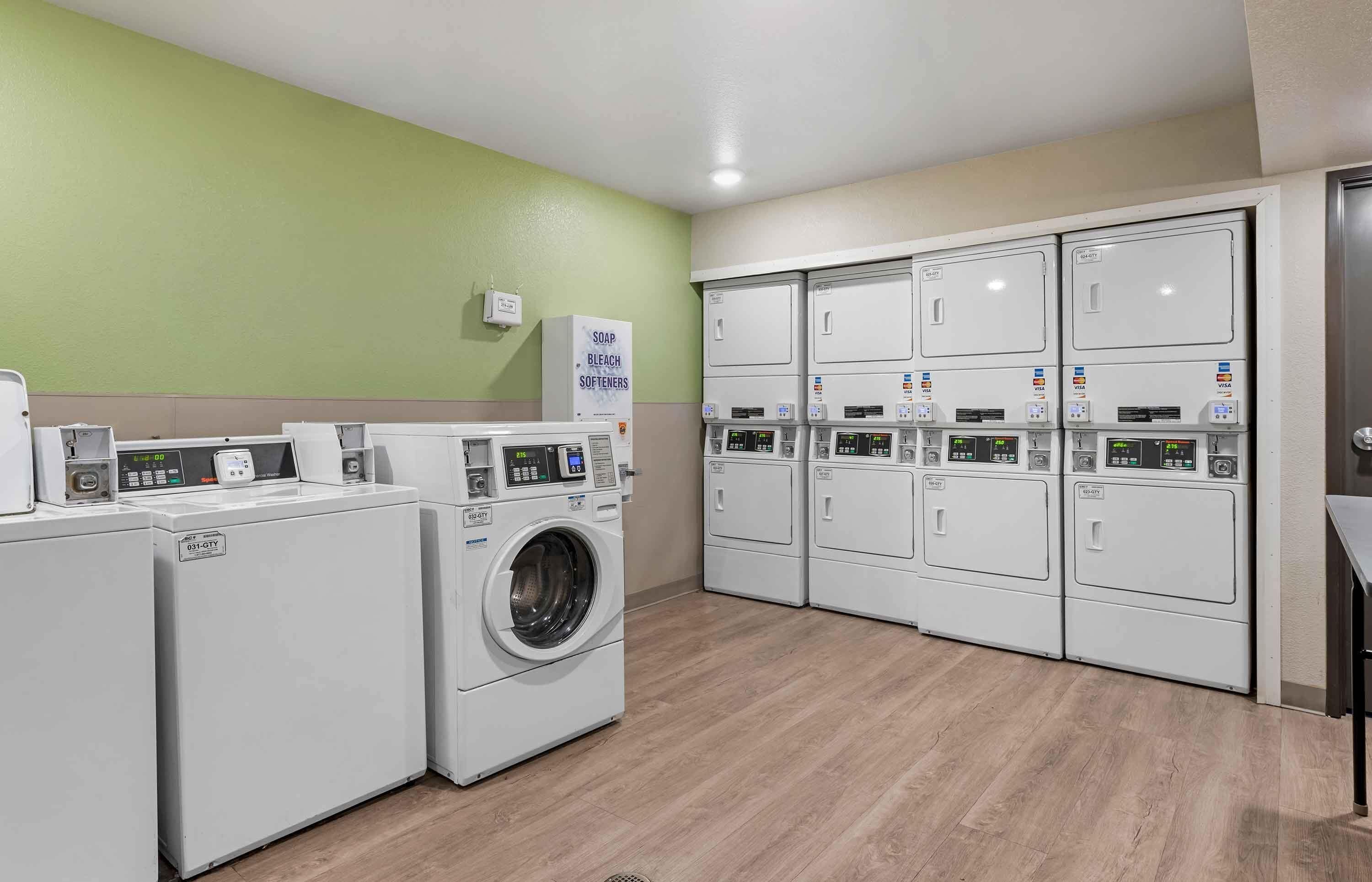 A laundry facility with multiple washing machines and dryers, a soap and bleach softener dispenser, and a digital display for each machine.