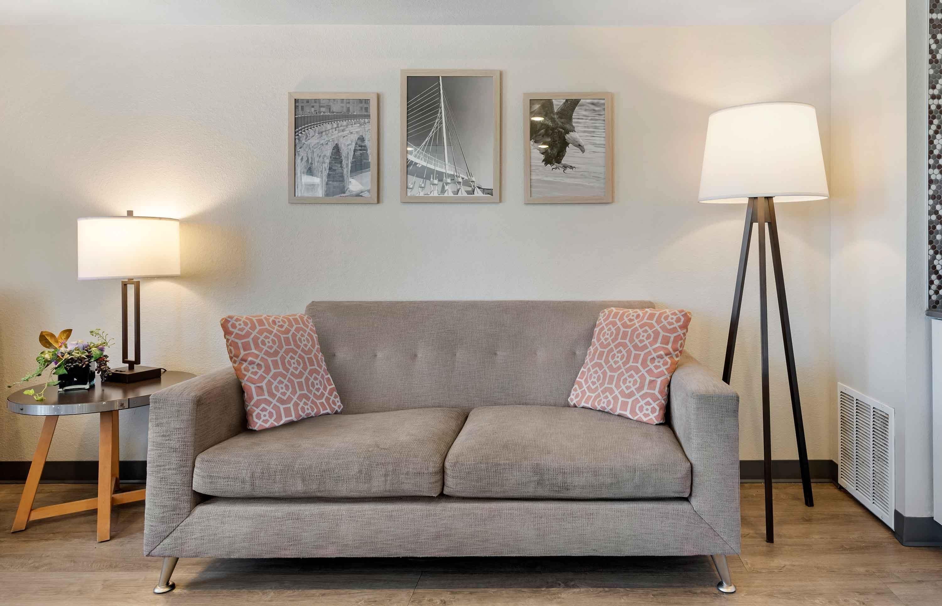 A neutral-toned sofa with patterned cushions, a small side table with a lamp and a vase of flowers, and three framed pictures on the wall.