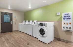A laundry facility with multiple washing machines and dryers, a no-smoking sign, and a poster advertising soap, bleach, and softeners. - Extended Stay America Suites - Minneapolis - Fridley (Fridley)