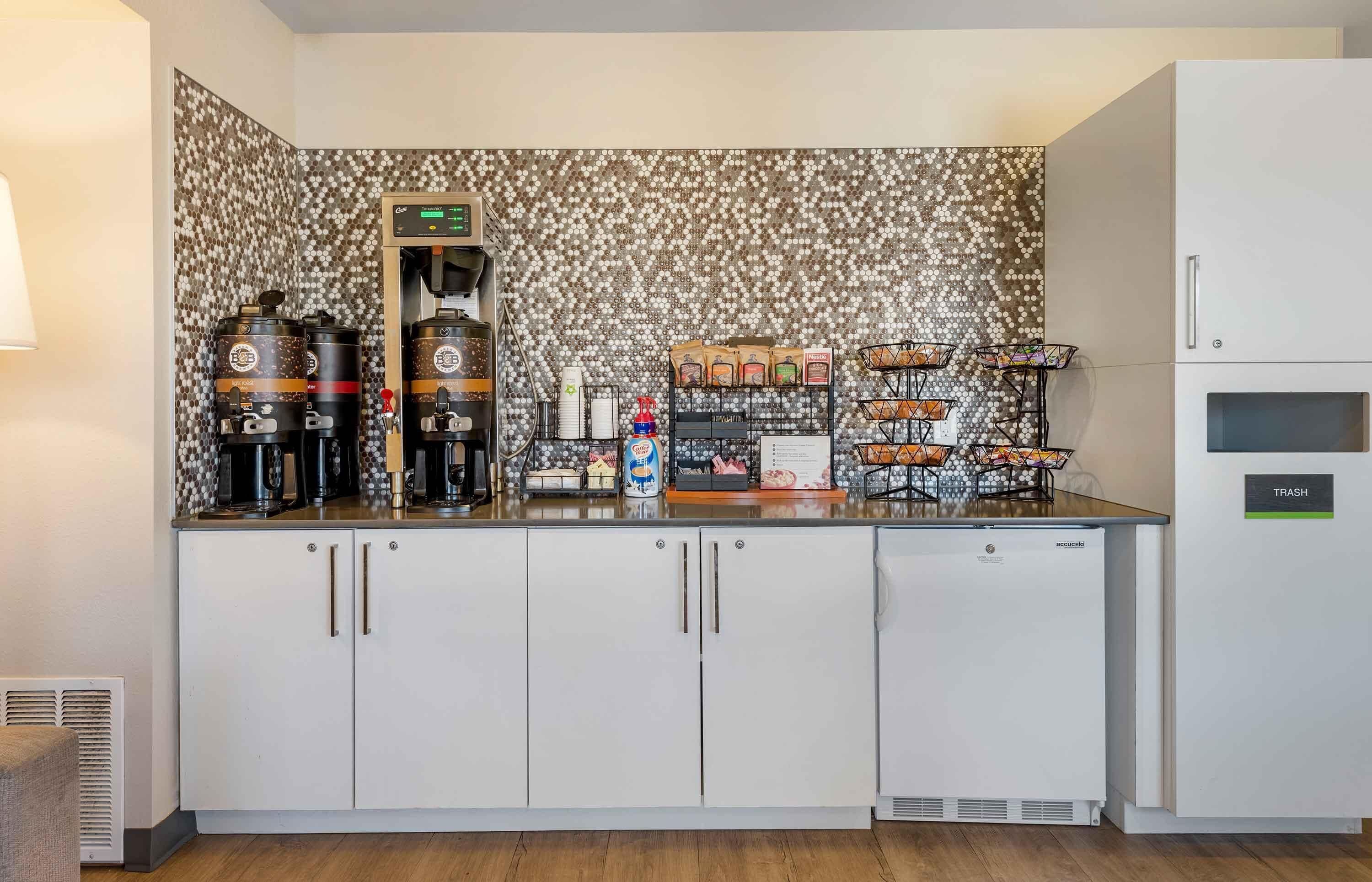Una kitchenette con cafetera, dos máquinas de espresso, una preparadora de café, un expositor para pan y un basurero.