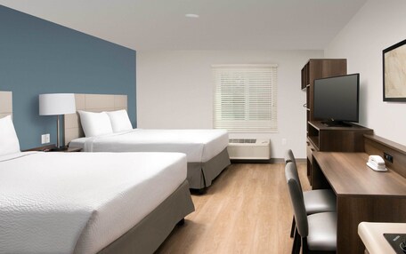 A hotel room with two beds, a desk, a chair, a TV, and a window with blinds.