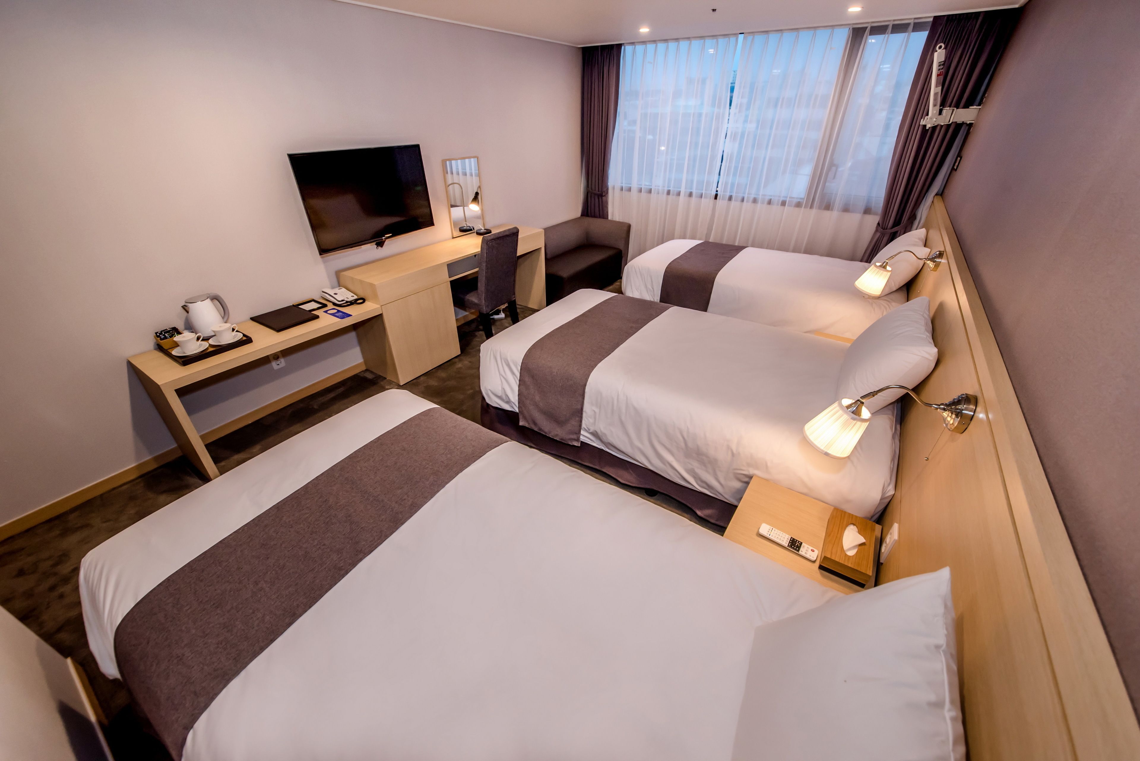 A hotel room with two beds, a desk, a television, and a window with curtains.