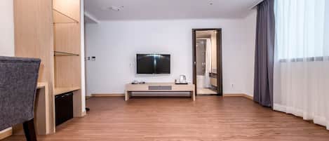 Ein modernes Hotelzimmer mit Holzboden, einem flachbildfernseher an der Wand, einem kleinen Tisch mit Wasserkocher und einem Kleiderschrank.
