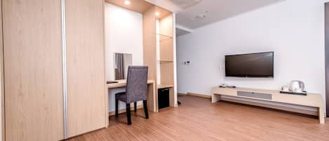 A modern hotel room with a wooden floor, a desk with a chair, a flat-screen TV mounted on the wall, and a bench with a cup and saucer.