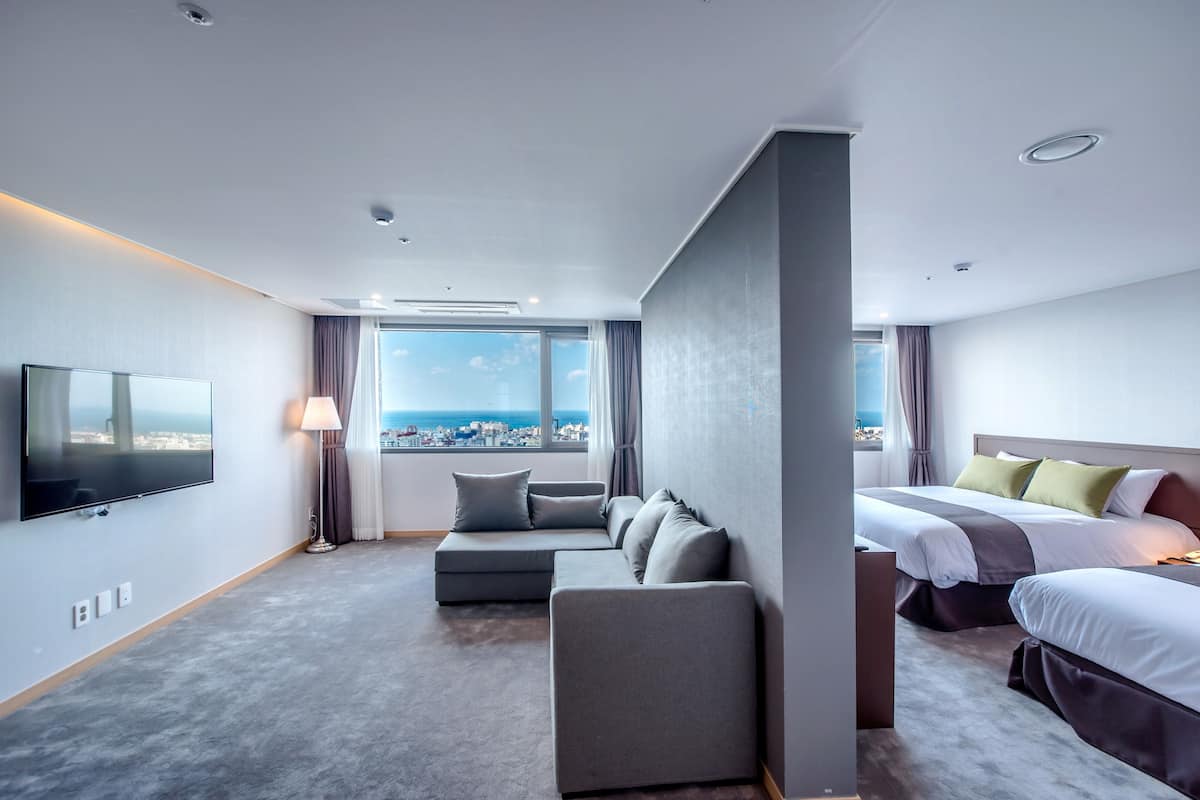 A modern hotel room with a large bed, a sofa, a TV, and a view of the city.