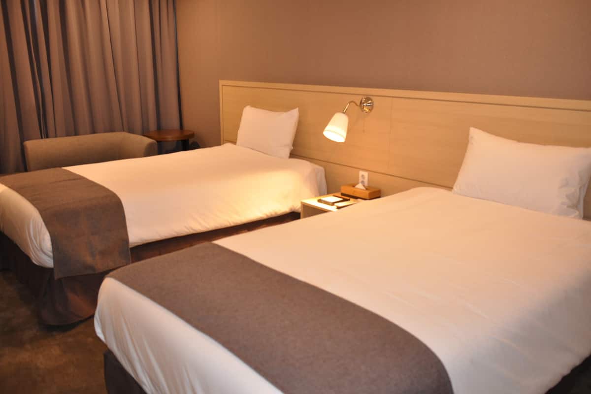 A hotel room with two beds, a nightstand, a lamp, and a curtain.
