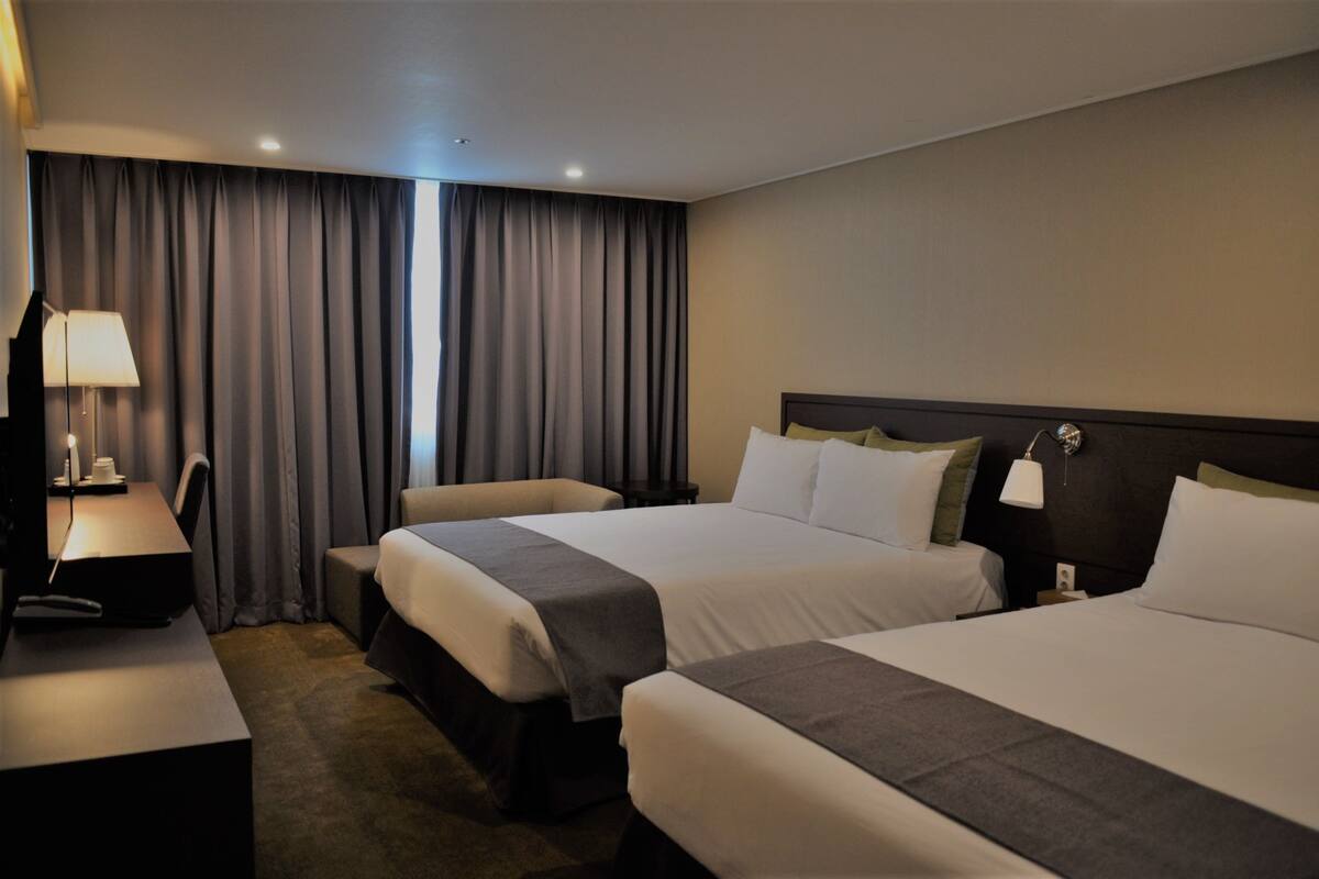 A hotel room with two beds, a desk, a lamp, and a TV.
