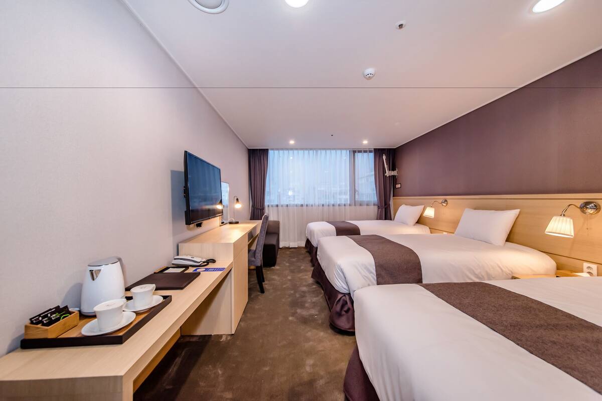 A hotel room with two beds, a desk with a coffee maker, a television, and a window with curtains.