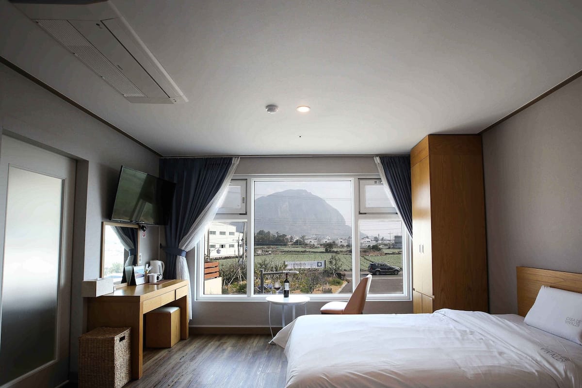 A hotel room with a bed, a TV, a desk, and a window with a mountain view.